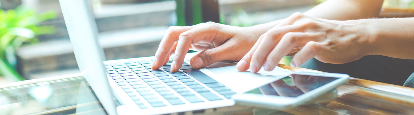 hands typing on laptop computer with cell phone sitting on table