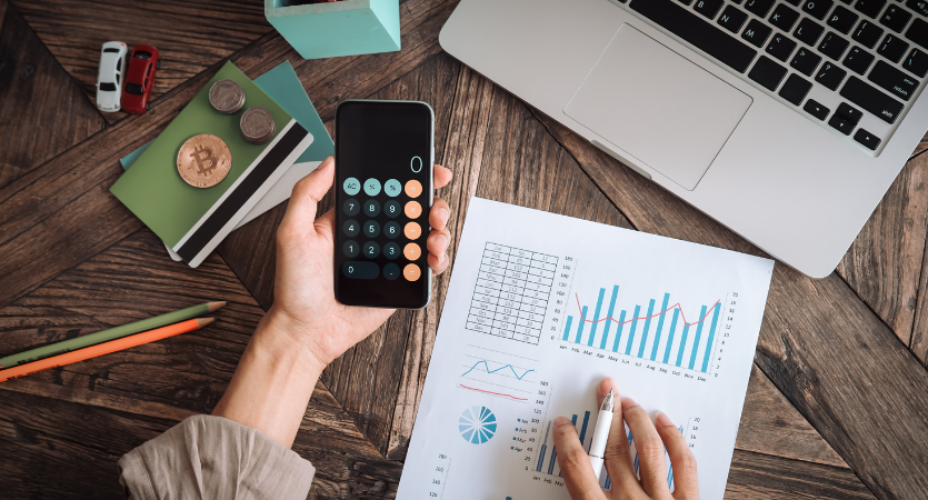 a hand holding a calculator hovering above paperwork on a desk