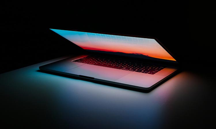 laptop computer half open with it's screen light shining on the top of the surface it's resting on
