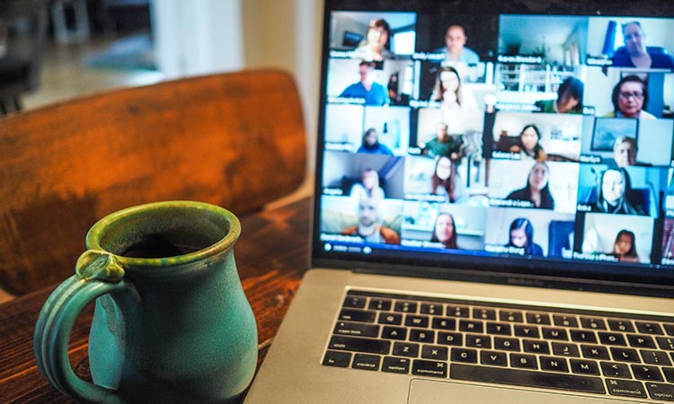 Kitchen table with a coffee cup and laptop open to a group teleconference meeting
