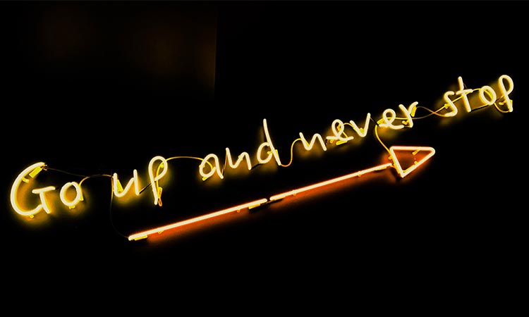 Neon sign stating Go Up and Never Stop with an arrow as an underline