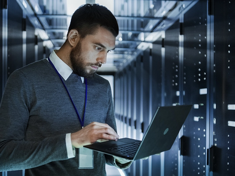 image of man in server room checking laptop computer